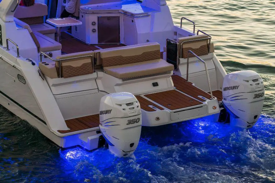 Luxury motorboat with two Mercury 350 engines and blue lighting, docked on calm water, featuring a spacious seating area.